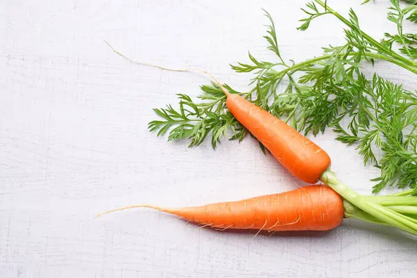 Beyaz ahşap arka planda yaprakları olan organik havuçlar..