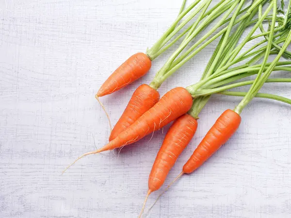 Beyaz ahşap arka planda yaprakları olan organik havuçlar..