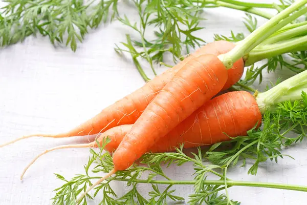 Beyaz ahşap arka planda yaprakları olan organik havuçlar..