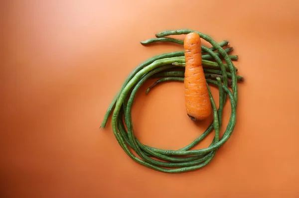Long beans and carrot isolated on orange background.