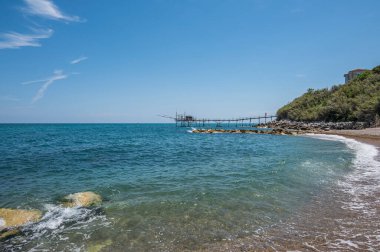 San Vito Chietino - 07-08-2022: Kristal berrak ve mavi denizi ve arka planda trabocco ile Calata Turchina 'nın güzel plajı