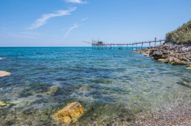 San Vito Chietino - 07-08-2022: Kristal berrak ve mavi denizi ve arka planda trabocco ile Calata Turchina 'nın güzel plajı