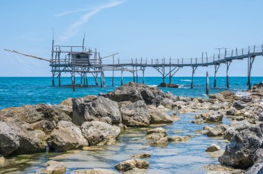 San Vito Chietino - 07-08-2022: Kristal berrak ve mavi denizi ve arka planda trabocco ile Calata Turchina 'nın güzel plajı