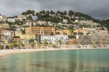 Menton 'un turkuaz suyu ve arka planda güzel renkli evleri olan güzel plajı.