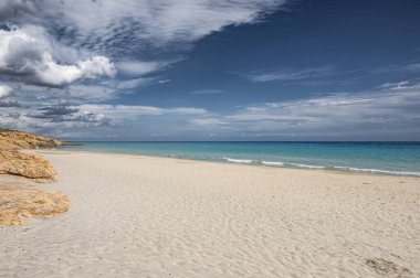 Sardunya 'daki güzel Pinus plajı. Ufukta kum, mavi ve turkuaz su ve fırtına bulutları var.