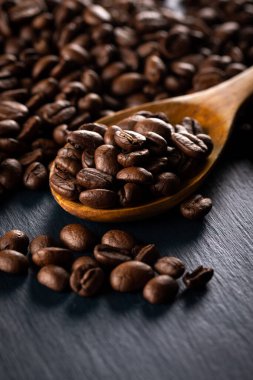 Koyu arkaplanda tahta kaşıkla kahve çekirdekleri..