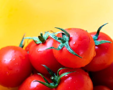 Sarı zemin üzerinde su damlaları olan kiraz domatesleri. Çeri domateslerini su damlalarıyla yıkadım.. 