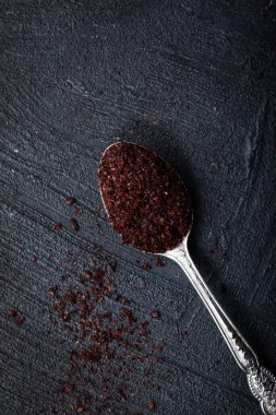 Geleneksel oryantal baharat sumac metalik kaşıkla koyu arkaplanda.