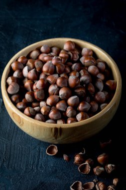 Hazelnuts in wooden bowl on dark background.