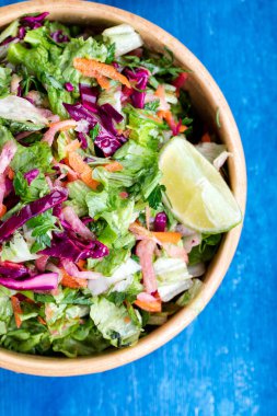 Mor lahanalı taze sebze salatası, beyaz lahana, marul ve havuç, mavi ahşap arka planda ahşap bir kasede. Üst görünüm.