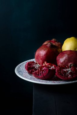 Siyah ahşap masada beyaz porselen tabakta taze sulu nar parçaları. Koyu arkaplanda taze meyveler.