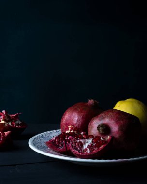 Eski kırsal masa üzerinde taze nar, koyu tonlarda durgun hayat. Olgun ve sulu nar meyveleri yakın plan siyah zemin üzerinde.