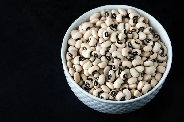 Black eye peas in a white bowl on black background, top view. Black-eyed beans, also known as cowpeas.