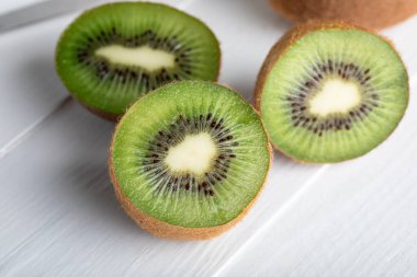 Beyaz ahşap bir yüzey üzerinde taze, yarı yarıya kivi görüntüsü. Canlı yeşil et ve küçük siyah tohumlar açıkça görülebilir, meyvelerin doğal dokusunu ve rengini sergiliyor..