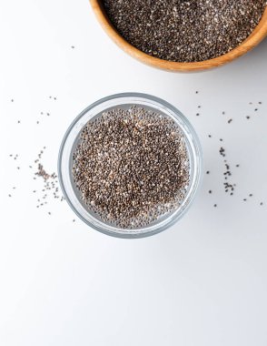 Suyla dolu bir bardakta Chia tohumu. Üst Manzara. Beyaz zemin üzerinde Chia tohumları olan bir bardak su..