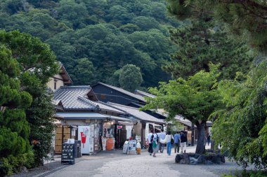 Kyoto 'nun Arashiyama bölgesinde, geleneksel ahşap evler ve gür orman tepeleri tarafından çerçevelenmiş büyüleyici bir ara sokak. 07.01.2025.
