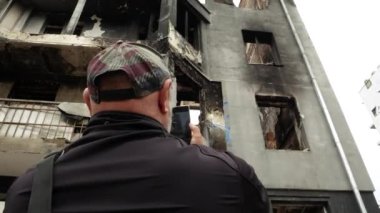 Bir adam akıllı telefondan ateş ediyor. Şehrin çok katlı binasını yakıp yıkıyor. Russo-Ukrayna Savaşı 2022. Rus ordusu barış dolu şehirlerin yerleşim yerlerini bombalıyor. İnsanlar karşı...