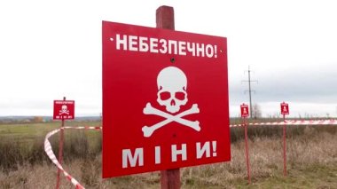 Üzerinde Tehlike Mayınlı yazan kırmızı uyarı işaretleri ve alanın ortasına bantlar iliştirilmiş. Rus-Ukrayna savaşı 2022. Rus ordusu Ukrayna topraklarına mayın döşedi. Mayınlar ve el bombası.