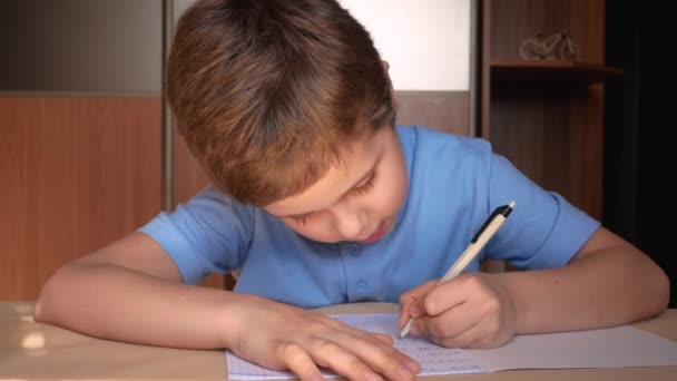 7歳のかわいい男の子が左手でノートにペンで書きます コヴィト 19流行期の遠隔教育 — ストック動画