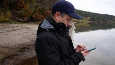 Sonbaharın sonlarında gölün kıyısında elinde akıllı bir telefonla ekranda kayan bir adam. Sosyal ağlarda iletişim. İnternet alışverişi. İnternet Bankacılık