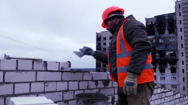 ハリコフ ウクライナ 11月 2022 オレンジのヘルメットとベストの建設労働者は 背の高いスタンド トロールとレンガの壁にセメントを置き 均等にレンガを敷設 住宅の建設 — ストック動画