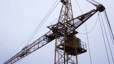 Mavi gökyüzüne çarpan büyük bir vinç. İnşaat alanında büyük makineler var.