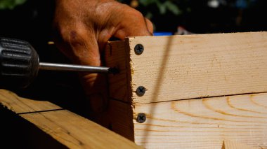 The master makes a wooden box. Screwdriver screws into a wooden board. Production of wooden tools for the garden