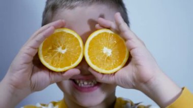 A cute child covers his face, eyes with sliced slices of cut orange, twirls them in front of his eyes