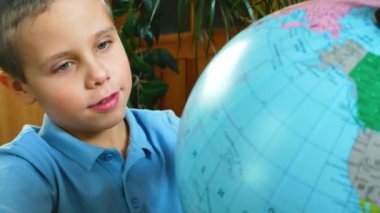 A cute boy spins the globe in front of him, looks for countries and continents and points his finger at the globe. The boy learns geography. Homeschooling. Study of countries. Passion for geography
