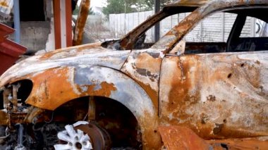 A burned-out passenger car in the yard of a private house. Rusted after the fire body. The Russian-Ukrainian war. Destruction in Ukrainian cities. Real video of the bombed village