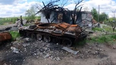Yanmış bir Rus tankı, bombardımanla yıkılan bir evin arka planına karşı. Ukrayna 'da gerçek savaş