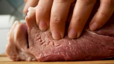 Female hands cut raw pork meat with a knife on a wooden board in the kitchen. Cooking meat dishes
