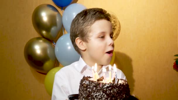 かわいい男の子が誕生日にケーキの上のろうそくを吹き消す 背景には多色の風船があります 子供の誕生日のお祝い — ストック動画