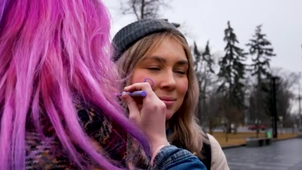 ウクライナのハリコフ 2023年3月8日ピンクの髪をした女の子が別の女の子の頬に性別のサインを描きます 女の子は男女平等と男女平等の権利のために戦います 男女共同参画の推進 — ストック動画