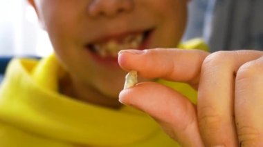 Bir çocuk yeni düşmüş süt dişini kameranın önünde tutuyor. Çocuklarda diş değişimi. Pediatrik dişçilik. Çocuklarda sağlıklı dişler. Arka planda, ön dişi olmayan gülümseyen bir çocuk.