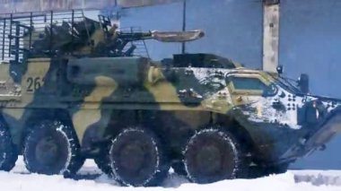 Ağır zırhlı bir personel taşıyıcı, karda hangar boyunca ilerliyor. Ağır askeri teçhizat savaş pozisyonlarına geçer. Rus-Ukrayna savaşı. Ukrayna için silah malzemeleri ve hazırlıkları