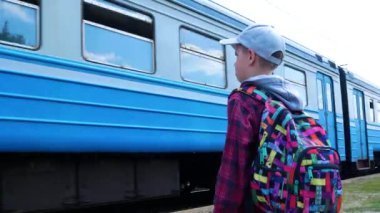 Kharkiv, Ukrayna - 5 Haziran 2022: Sırt çantalı bir çocuk, platformda duruyor ve giden trene bakıyor. Seyahat konsepti. Demiryolu raylarını nasıl geçeceğiz?
