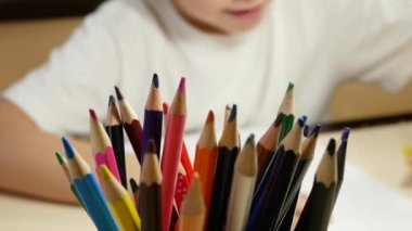 Bir anaokulu çocuğu kalemle resim çizer. Ön planda kalemler var.