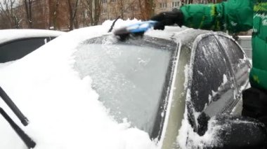 Bir adam bir arabanın ön camından kar temizliyor. karlı kış
