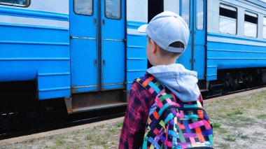 Omuzlarının üzerinde sırt çantası olan 8-9 yaşlarında bir çocuk tren istasyonunda duruyor ve giden trene bakıyor. Rusya-Ukrayna savaşı sırasında nüfusun tahliyesi