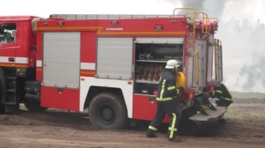 Kharkiv, Ukrayna - 29 Mayıs 2021: İtfaiyeciler hortumlarını gevşetip yangını söndürmek için koşuyorlar. Ön planda bir itfaiye aracı var. Arka planda yangın, duman, ağaçlar