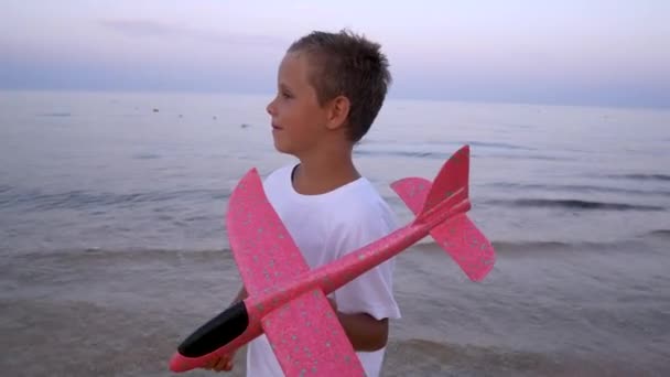 快乐的男孩6 日落时分 他手里拿着一架红色的飞机在大海的背景下 儿时的梦想男孩的飞行梦想 — 图库视频影像