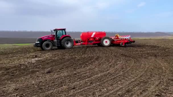 ウクライナのハリコフ 2023年4月17日 種を蒔いたトラクターが畑を走り 耕された準備された土地で小麦を蒔く 背景には黒い肥沃な丘陵地と曇りの空が描かれています — ストック動画