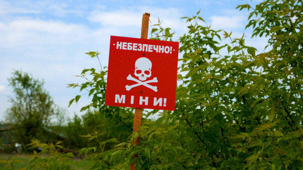 Красная табличка с черепом рядом с полевой дорогой, на которой написано "Осторожно, мины". Предупреждение об опасности мин. Война 2022-2023 годов. Территории были заминированы после военных действий. Концепция гуманитарного разминирования