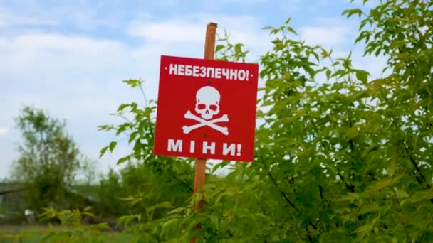一条红色的骷髅斑块靠近田野的路上 上面写着警告 地雷危险警告 2022 2023年战争 敌对行动后布雷的领土 人道主义排雷的概念 — 图库视频影像