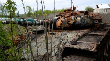 Çalılıklarda harap olmuş, harap olmuş, yanmış, paslı bir tank duruyor. Tankın namlusu yola doğrultulmuş durumda. Rus-Ukrayna Savaşı 2022-2023