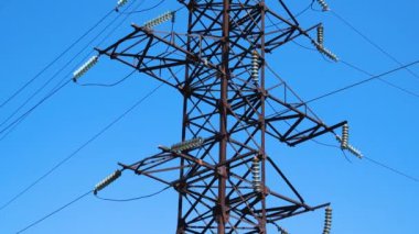 Mavi gökyüzüne karşı yüksek voltajlı elektrik hattından oluşan büyük metal bir direk. Elektrik üretimi ve taşımacılığı. Elektrik tarifeleri