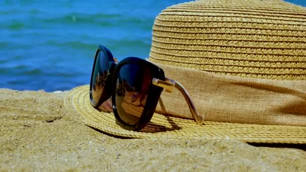 太阳镜和一顶草帽在沙滩上 映衬着大海的背景 海上娱乐的概念 — 图库视频影像
