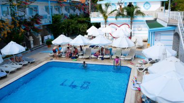 Taraf, Türkiye - 18 Haziran 2023: İnsanlar otelin havuz başında dinleniyor. Küçük bir çocuk havuzun kenarında yürür. Yukarıdan bak. Yaz tatili, sıcak yaz havuz kenarında, dinlenme.