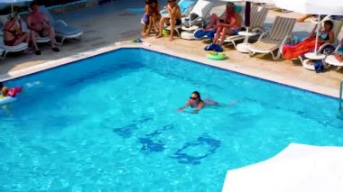 Side, Turkey - 22 Haziran 2023: Sıcak bir yaz gününde bir kız havuzda yüzer. Yakınlarda, çocuklar şişme dairelerde yüzerler. Yazın havuz kenarında aile tatili..